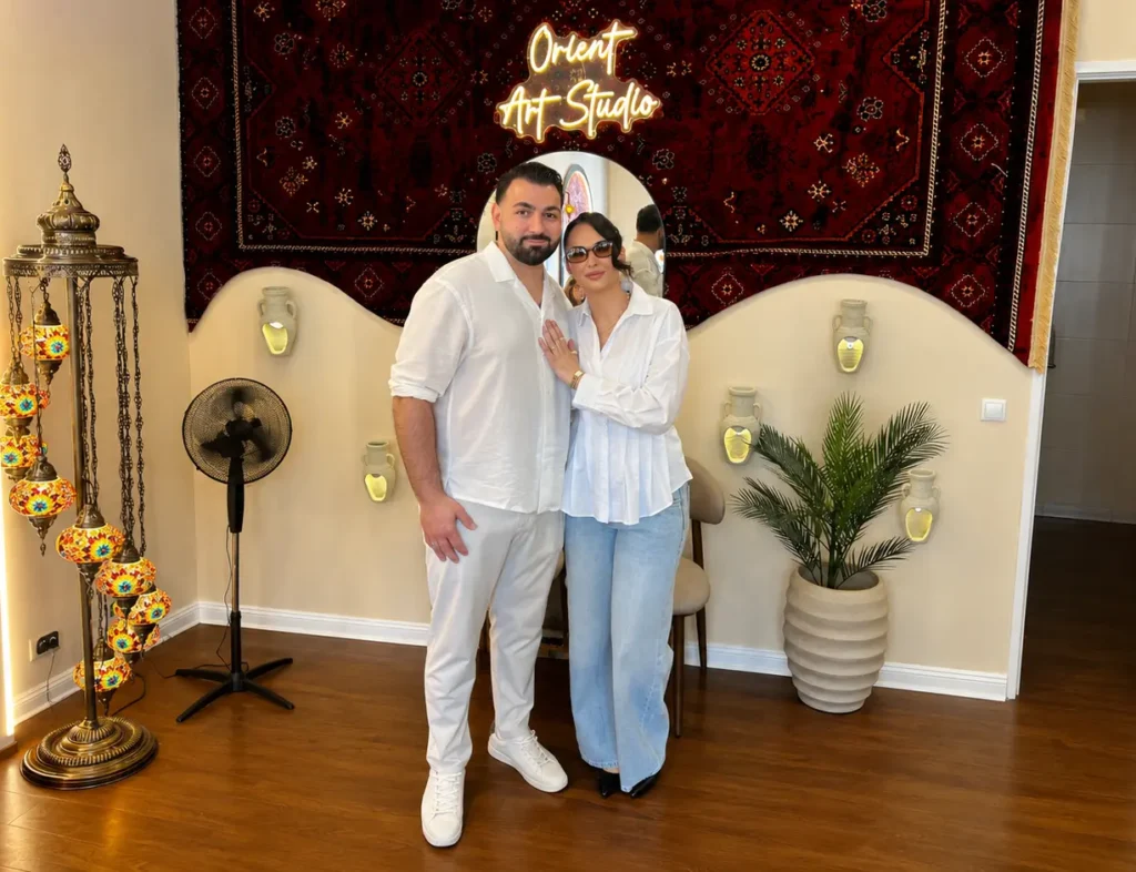 Ferhat and Dilara Taşkın in front of Orient Art Studio in Berlin with oriental decor and a glowing studio sign.